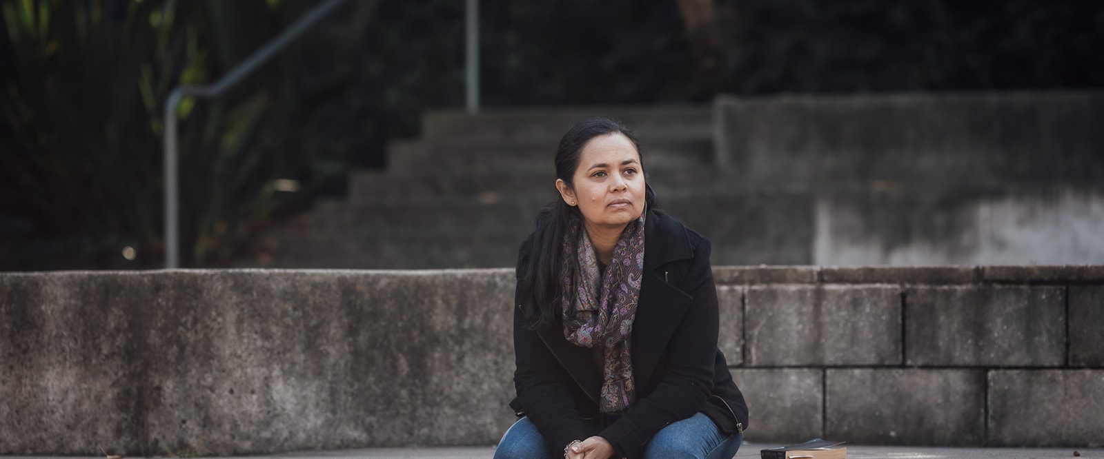 A woman sitting on a park step looking deep in thought.