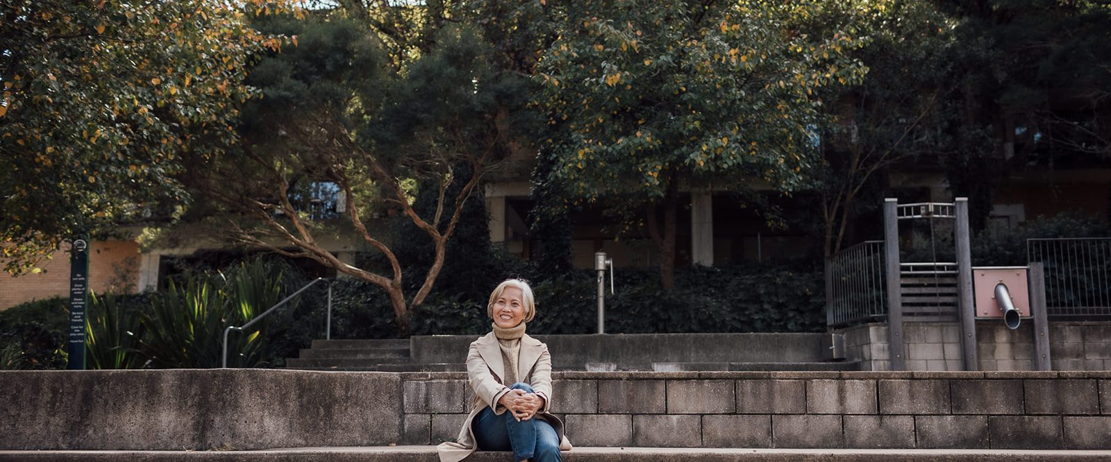 A woman sitting on a park step in nature, smiling.