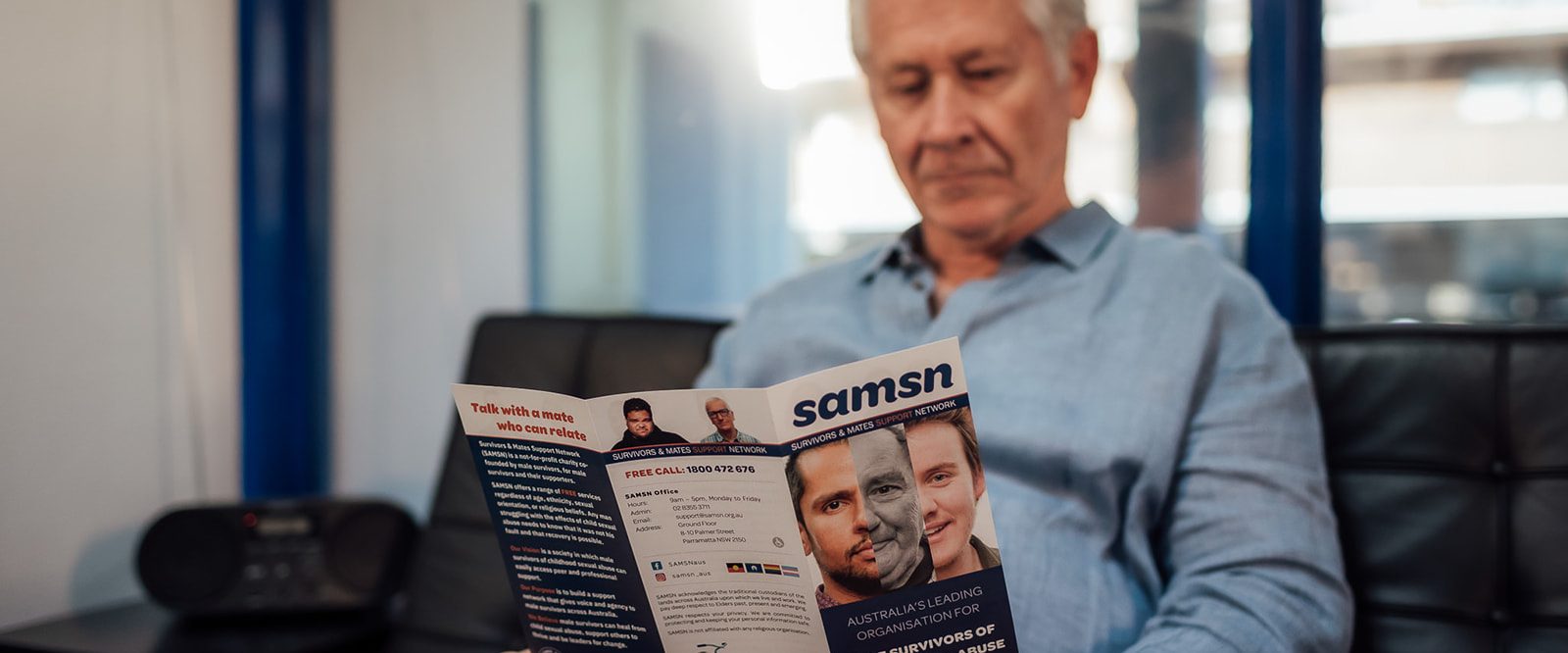 An older man sitting on a sofa reading a SAMSN brochure.